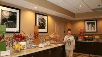 A buffet counter with various food items, a person standing, and framed pictures on the wall.