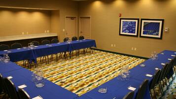 Una sala de conferencias con una larga mesa cubierta con manteles azules, sillas dispuestas alrededor y una alfombra estampada.