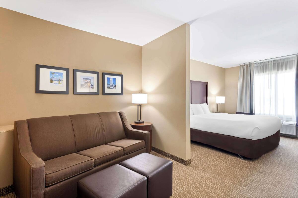 Ein Hotelzimmer mit braunem Sofa, einem kleinen Tisch mit Lampe, einem Bett mit weißer Bettwäsche und zwei gerahmten Bildern an der Wand.