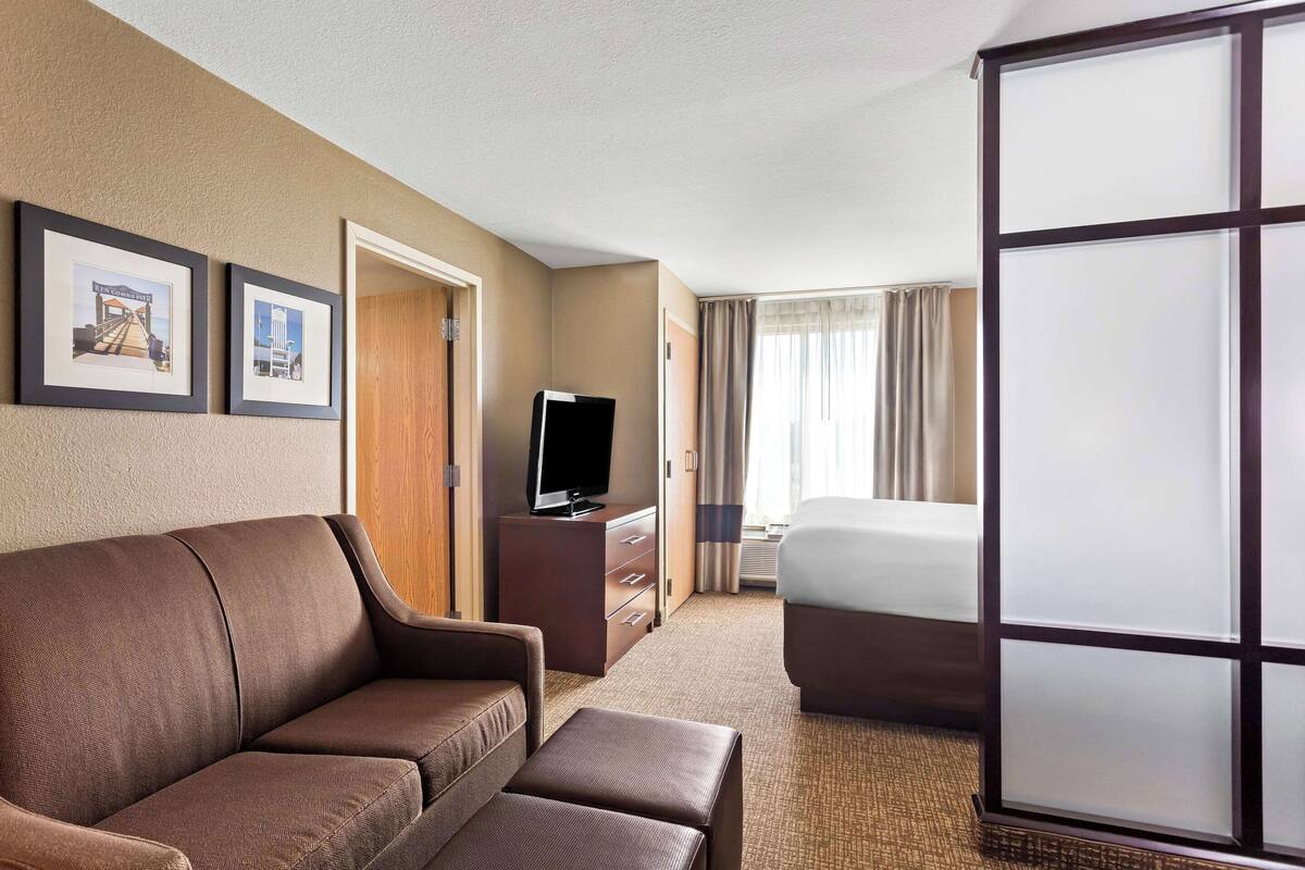 Ein Hotelzimmer mit einer Couch, einem Fernseher auf einer Holzkommode, einem Bett und einer Schiebetür.
