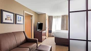 A hotel room with a sofa, a TV on a wooden cabinet, a bed, and a sliding door.