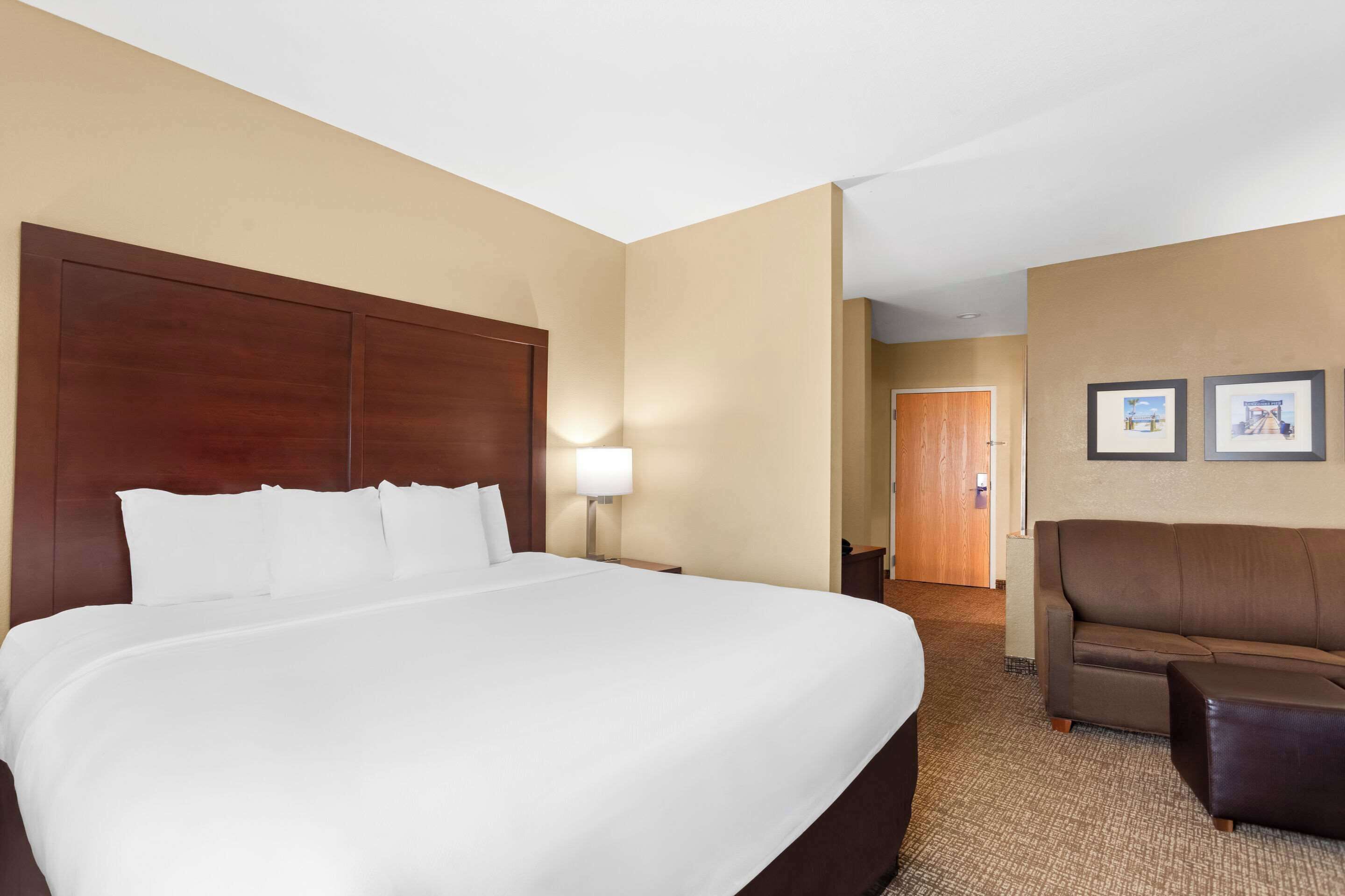 A hotel room with a large bed, a sofa, a lamp, and framed pictures on the wall.