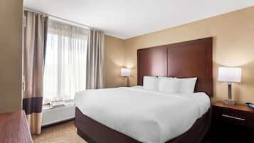 Una habitación de hotel con una cama grande, dos lámparas de noche, una mesita de noche de madera, un escritorio y una ventana con cortinas.