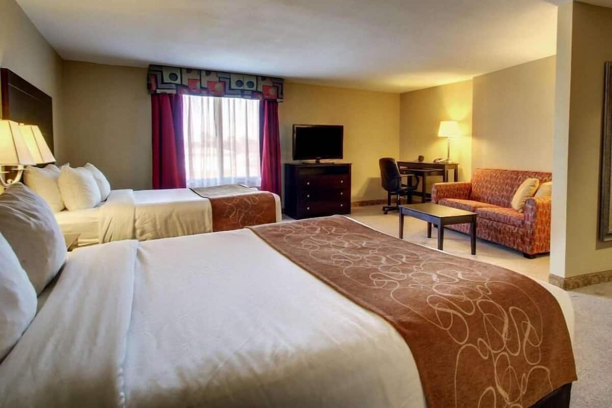Ein Hotelzimmer mit zwei Betten, einem Fernseher, einem Schreibtisch, einem Sessel und einer Couch.