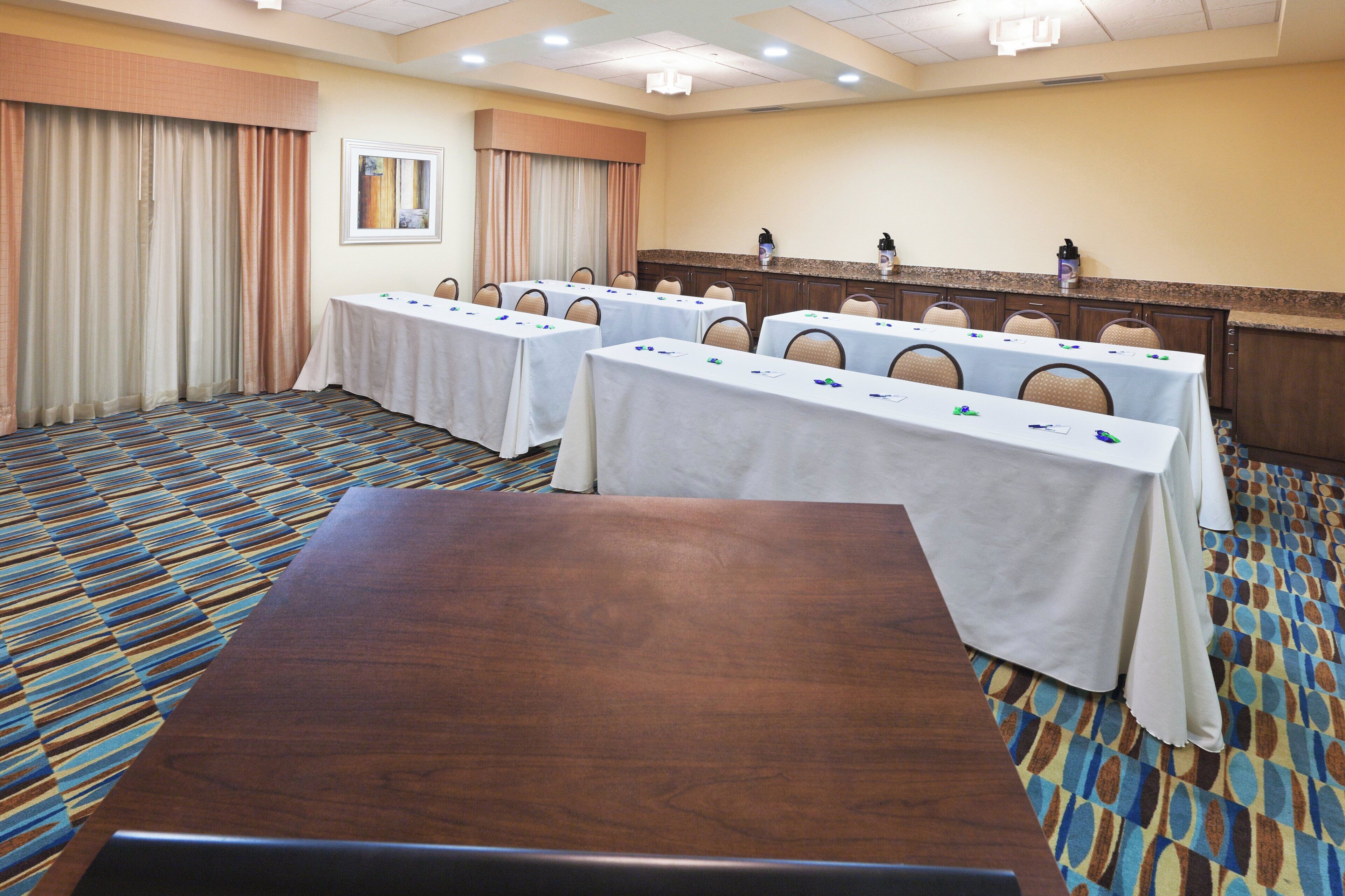 A conference room with multiple tables, chairs, and a large wooden table in the foreground.