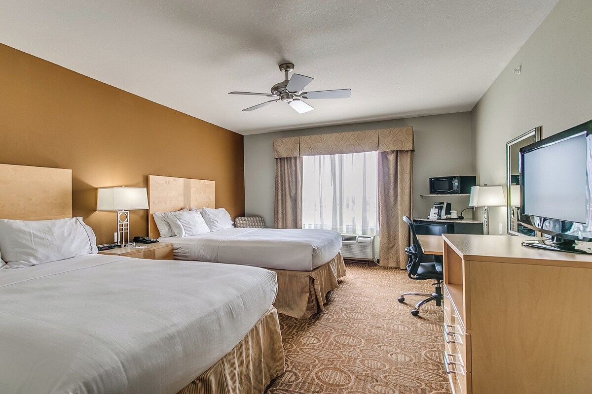 A hotel room with two beds, a desk with a computer, a television, and a ceiling fan.