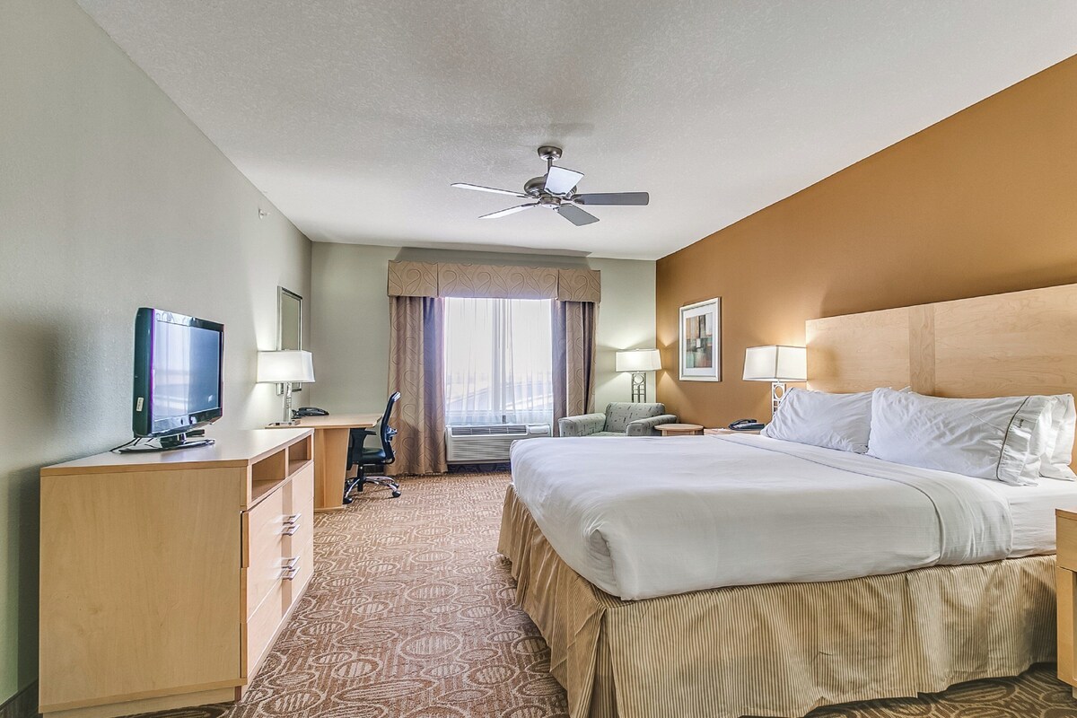 A hotel room with a bed, desk, chair, television, and a ceiling fan.
