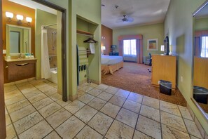 A hotel room with a bathroom, a bed, a desk, and a TV.