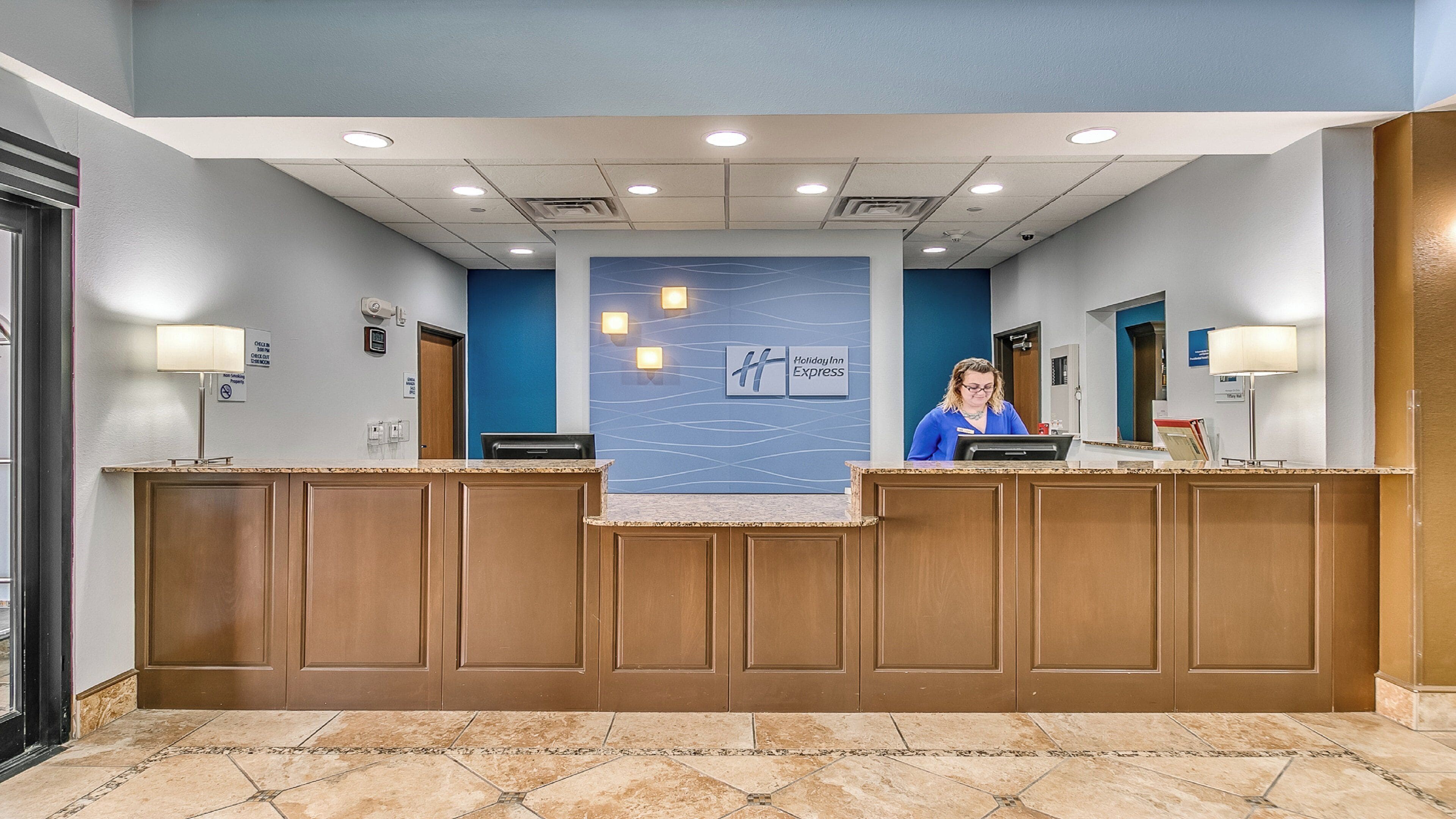 Un mostrador de recepción de hotel con una pared azul, una recepcionista y un letrero de Holiday Inn Express.