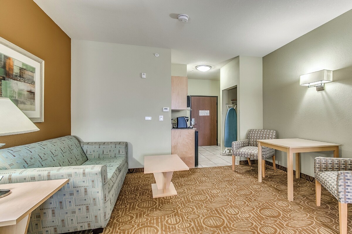 A hotel room with a sofa, armchair, small table, and a patterned carpet.