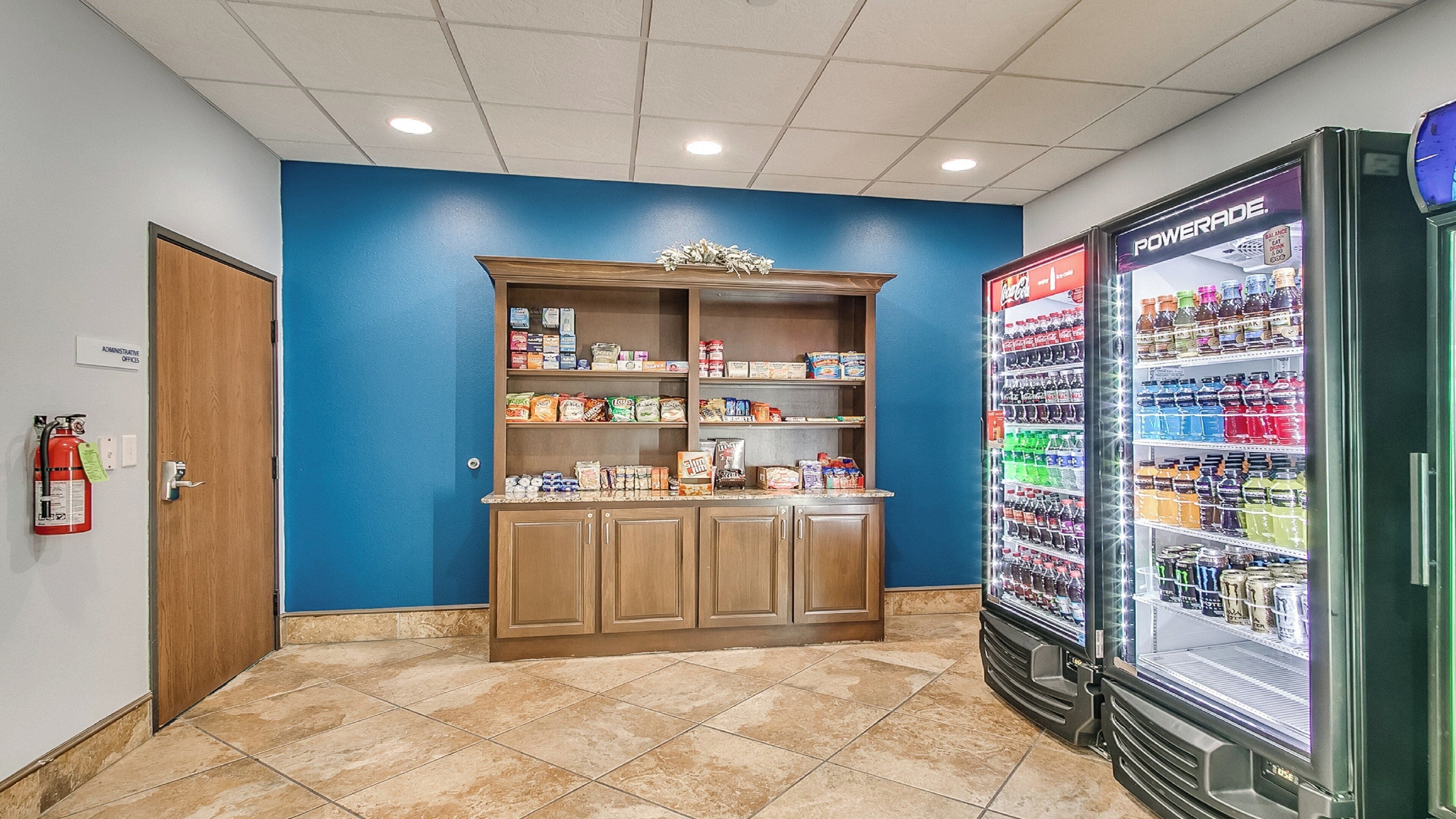 A kitchenette with a blue wall, a pantry with food items, and a beverage dispenser.