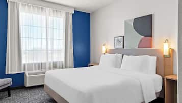 Una habitación de hotel con una cama grande, una ventana con cortinas blancas, un cuadro abstracto colgado en la pared y dos lámparas de noche.