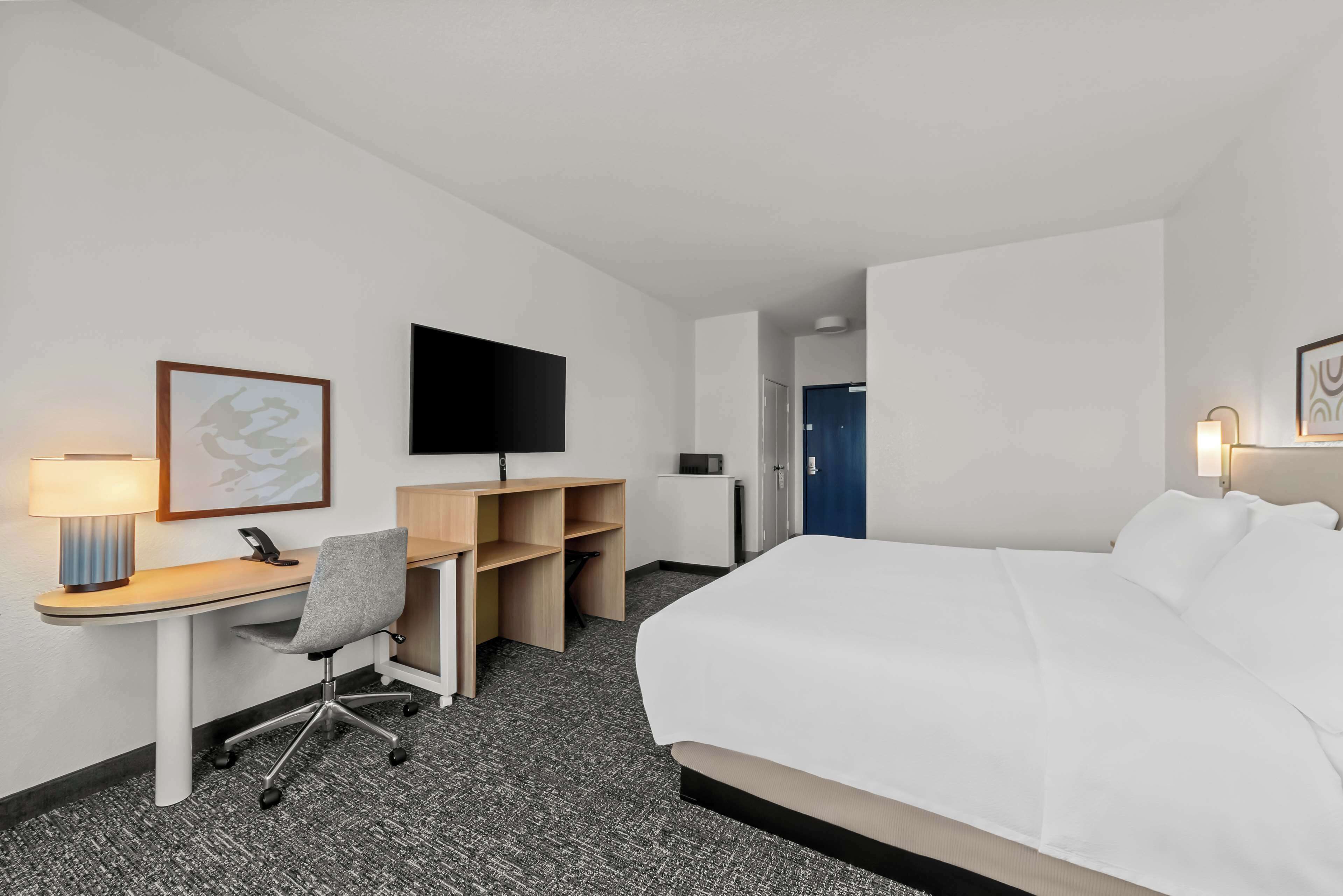 Una habitación de hotel con cama, escritorio, silla, televisor y puerta.