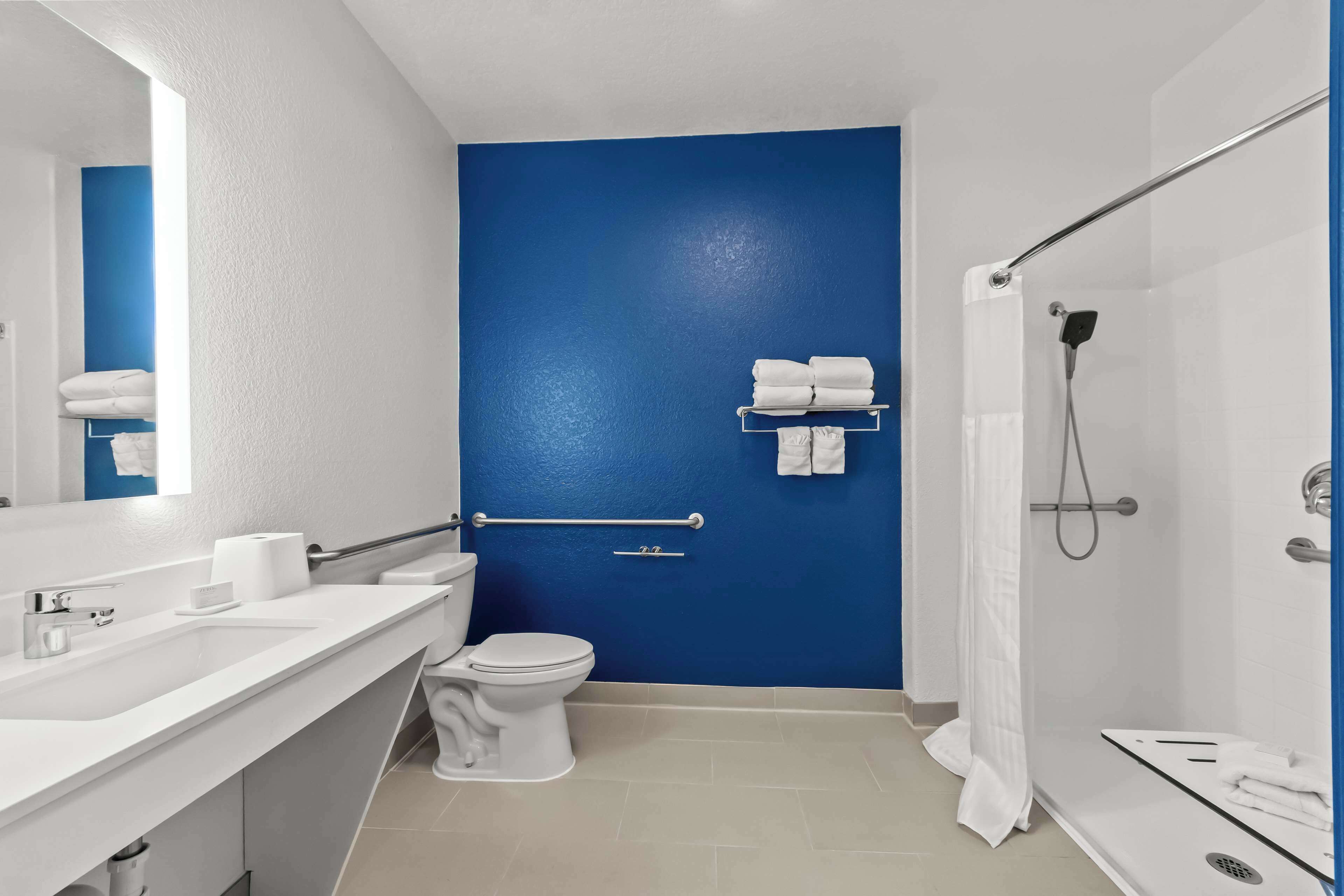 Un baño moderno con una pared de acento azul, un lavabo blanco, un inodoro y una zona de ducha.