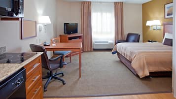 A hotel room with a bed, desk, chair, television, microwave, and air conditioning unit.