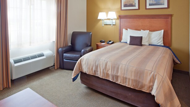 A hotel room with a large bed, a chair, a desk, and a window with curtains.