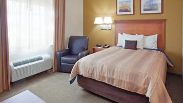 A hotel room with a bed, a chair, a desk with a phone, and a heater.