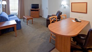 A hotel room with a sofa, a wooden desk, a television, a chair, and a small table.