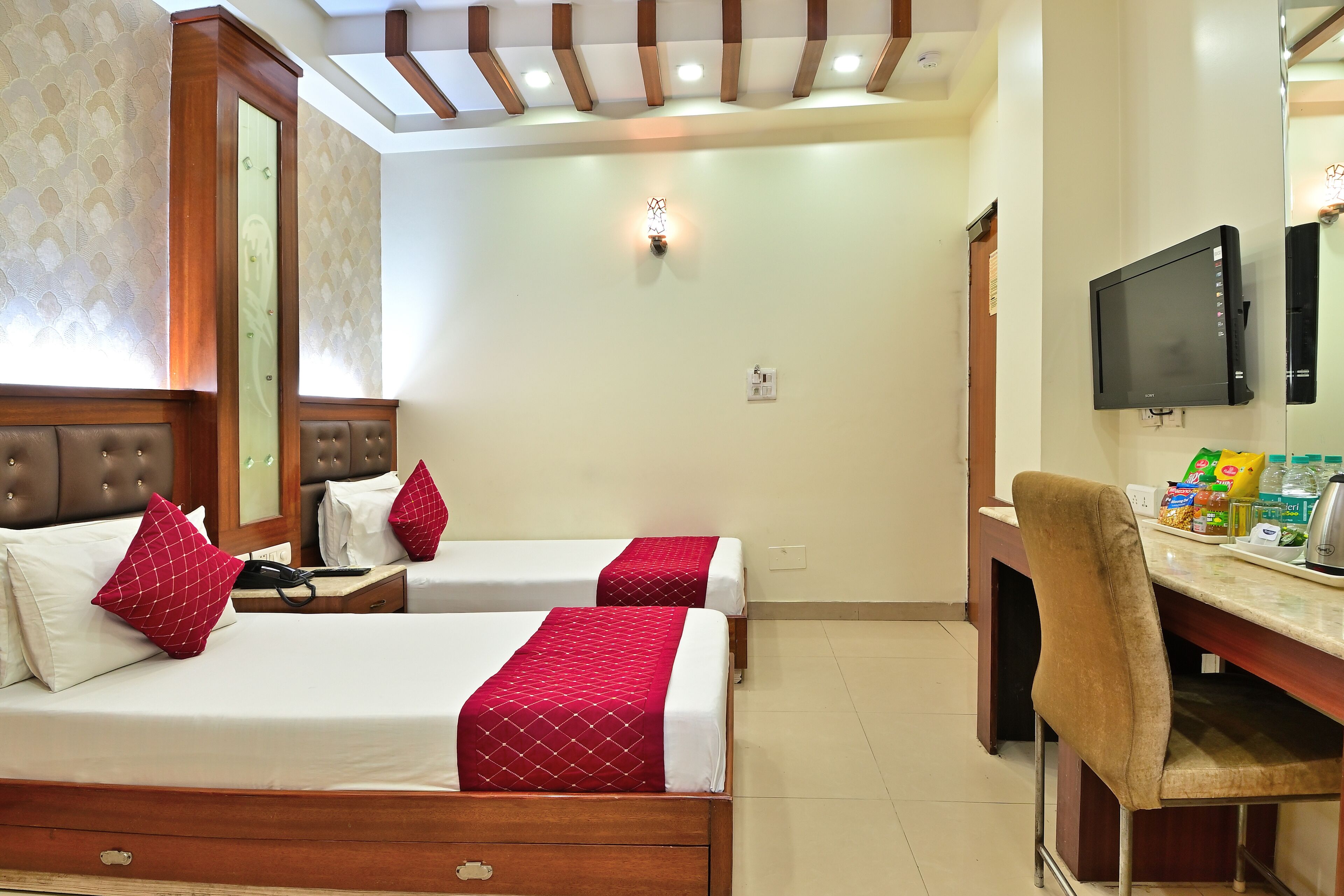 A hotel room with two beds, a desk with a chair, a television, and a small kitchenette.