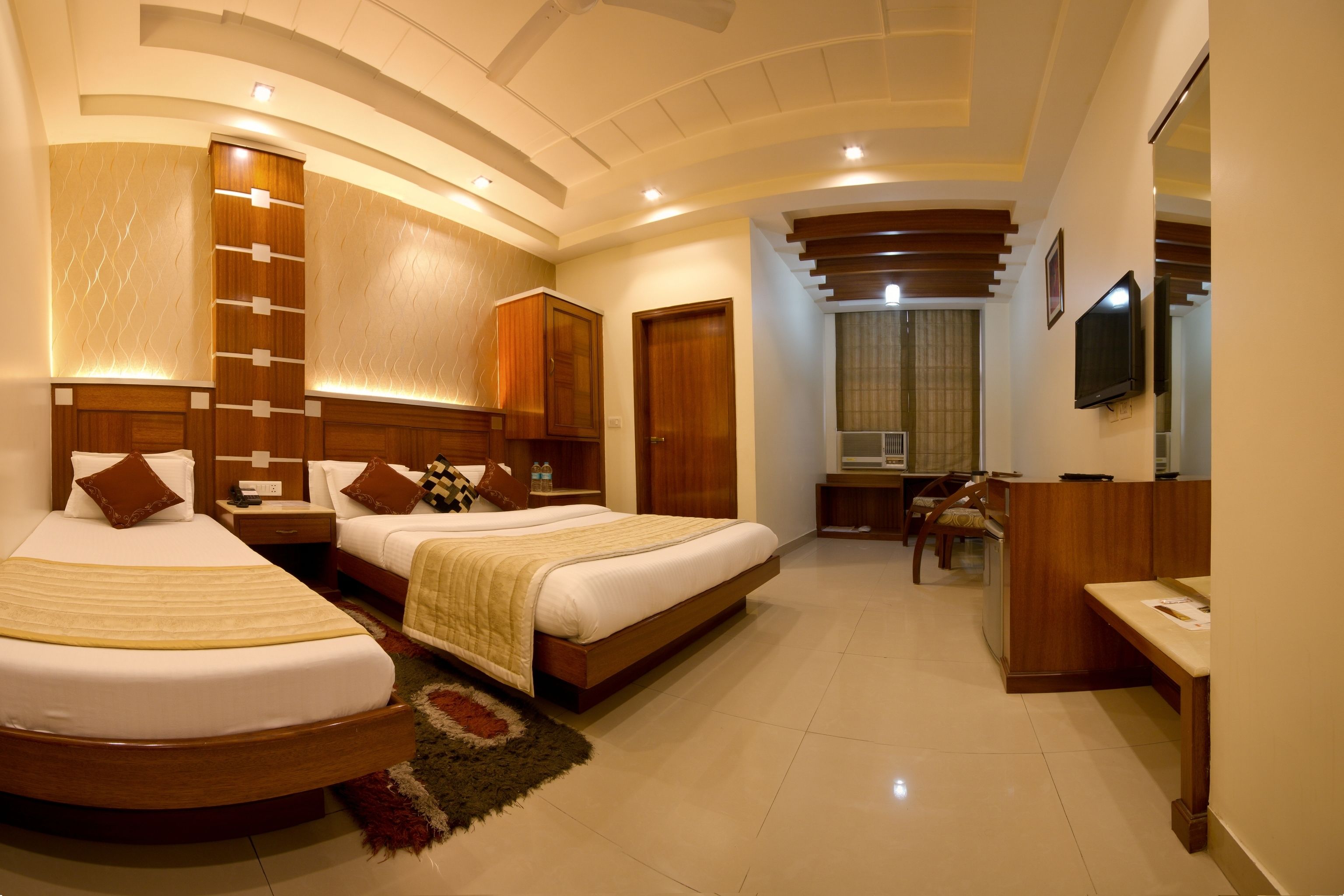 A hotel room with two beds, a desk, a TV, and a bathroom.