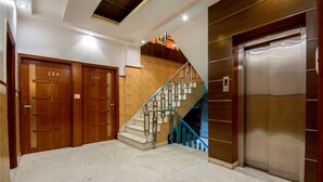 En hotellobby med et marmorgulv, mahognitrædøre med skiltene 124 og 125, en trappe med blå gelændere, og en moderne elevator.