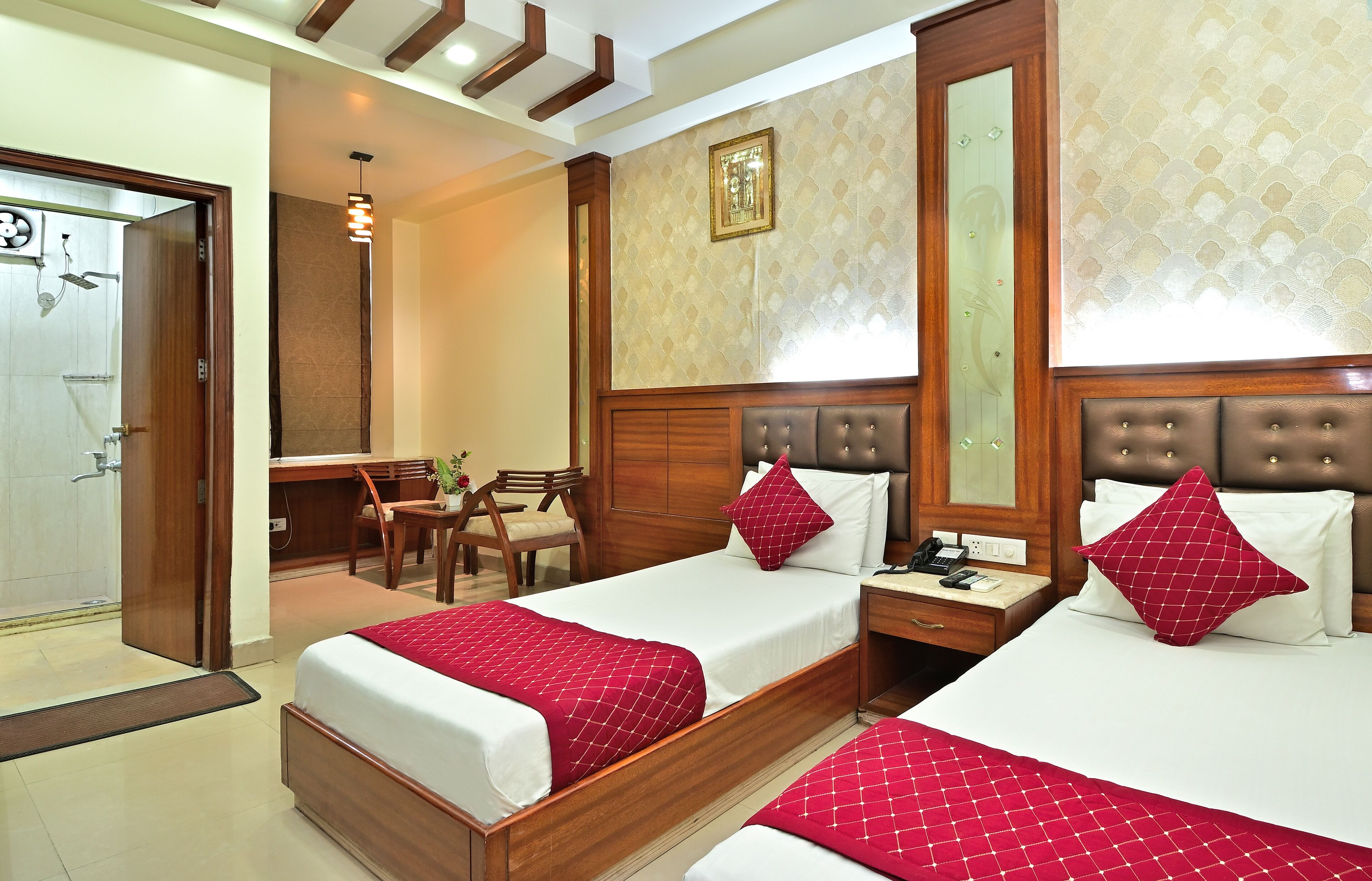 A hotel room with two beds, wooden headboards, a desk, and a chair.