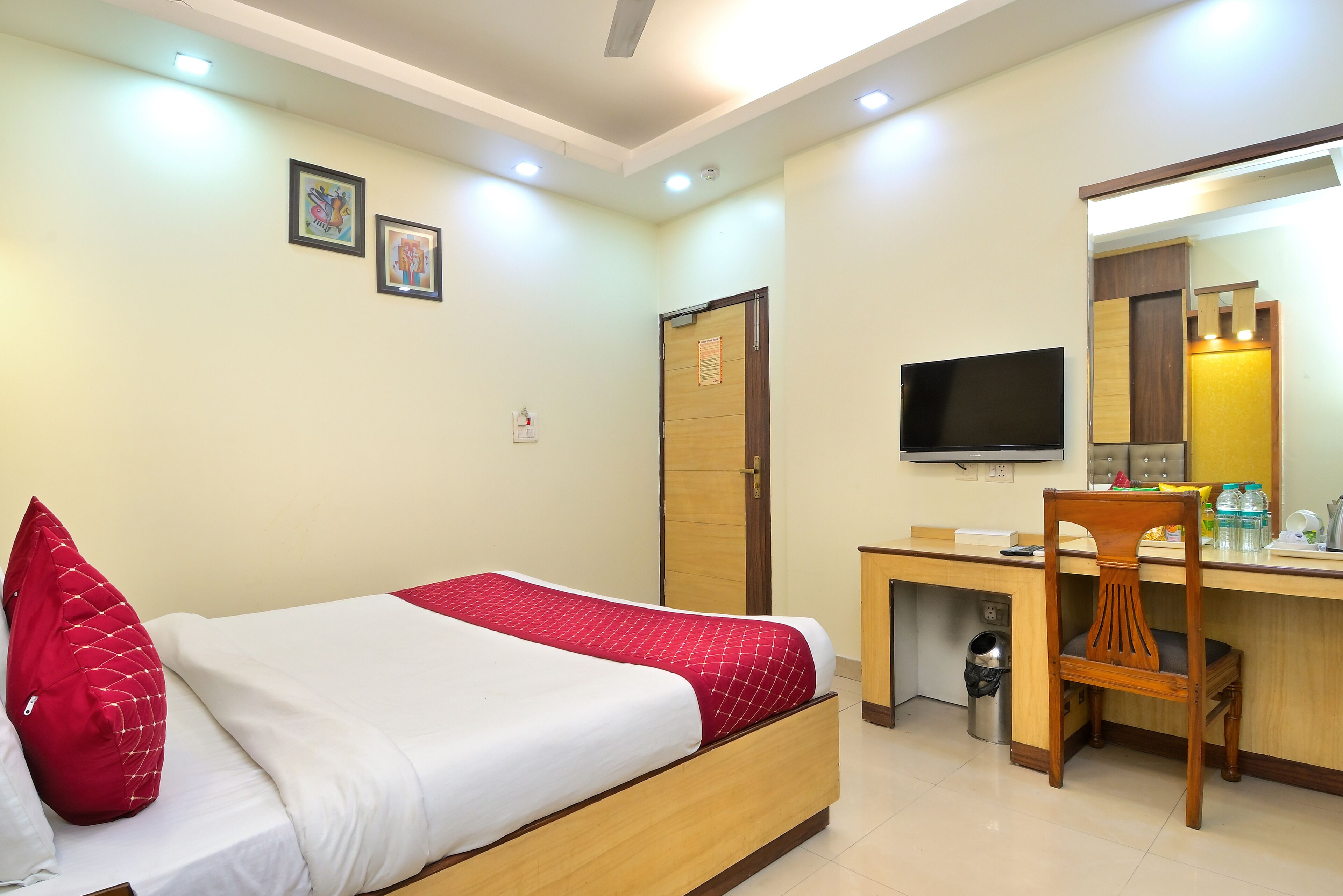 Una habitación de hotel con cama, escritorio, silla, televisor y un cubo de basura.