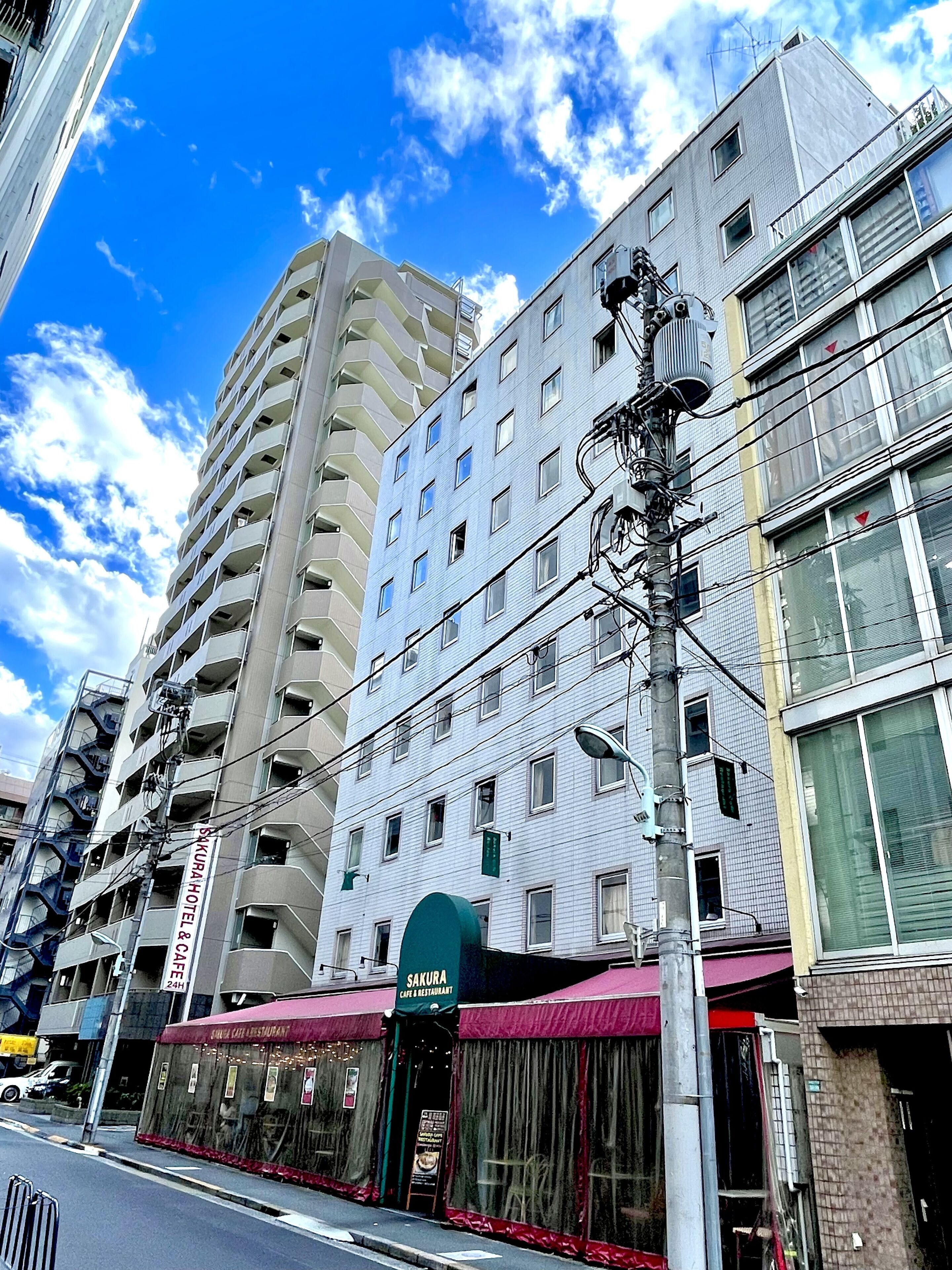 A multi-story building with a cafe and restaurant on the ground floor, a tall adjacent building, and a street with a traffic light.