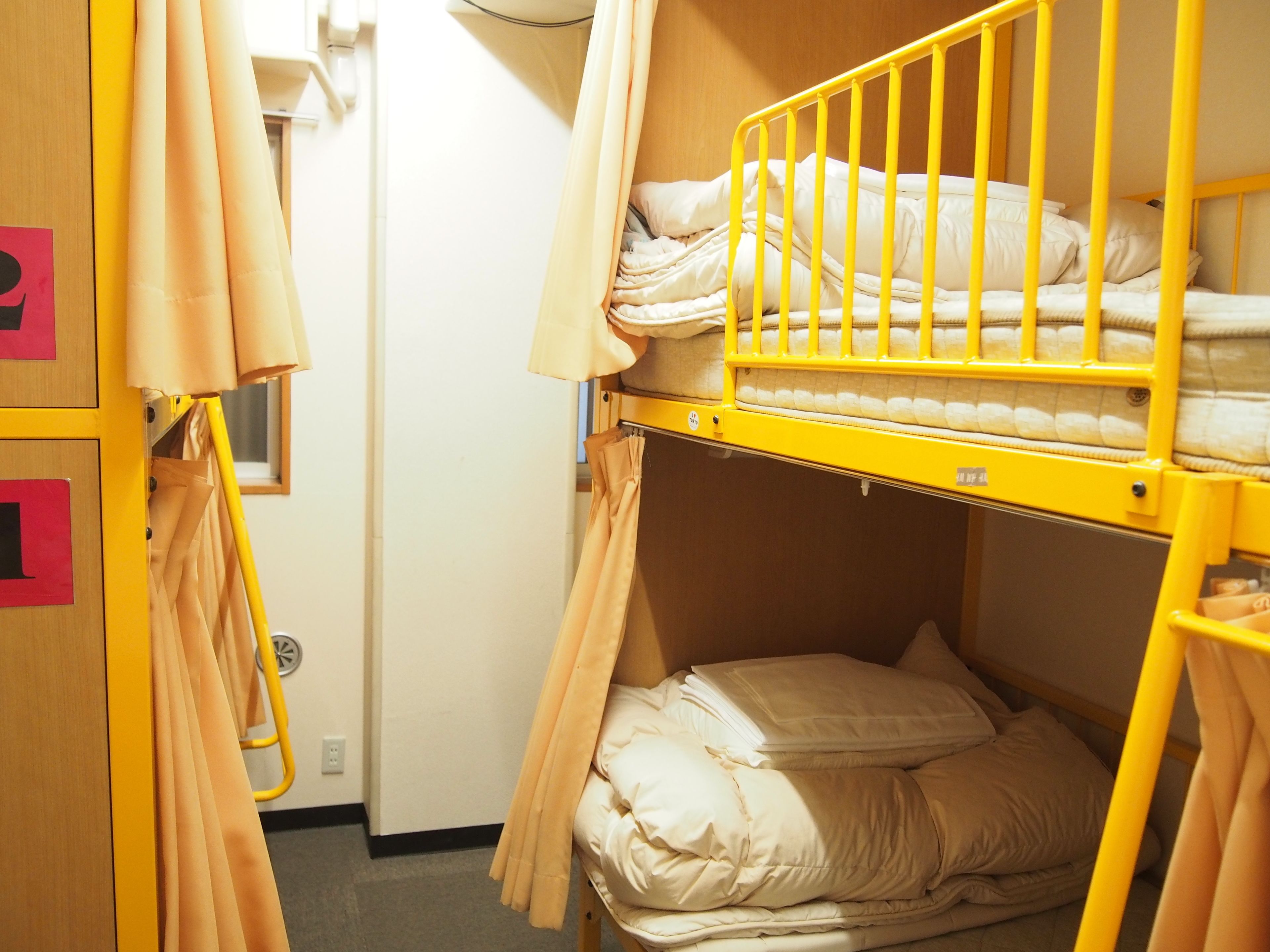 A bunk bed room with yellow railings, beige bedding, and a wooden wardrobe with red handles.