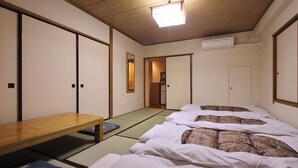 A traditional Japanese room with tatami flooring, a wooden table, and futon beds. - Sakura Hotel Ikebukuro - Hostel (Tokyo)