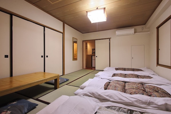 A traditional Japanese room with tatami flooring, a wooden table, and futon beds. - Sakura Hotel Ikebukuro - Hostel (Tokyo)