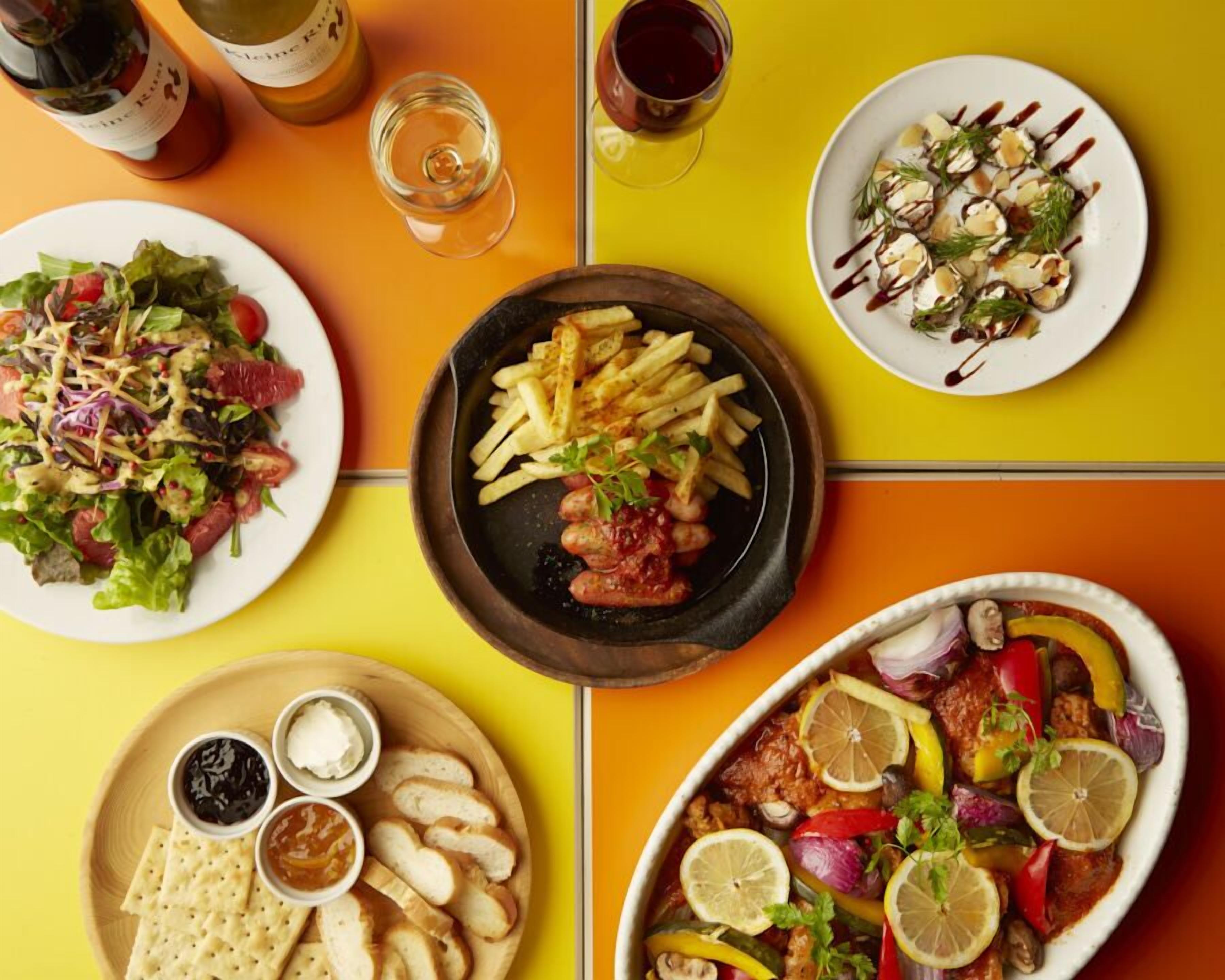 A table with various dishes, including a salad, fries, and a meat dish, along with drinks and bread.