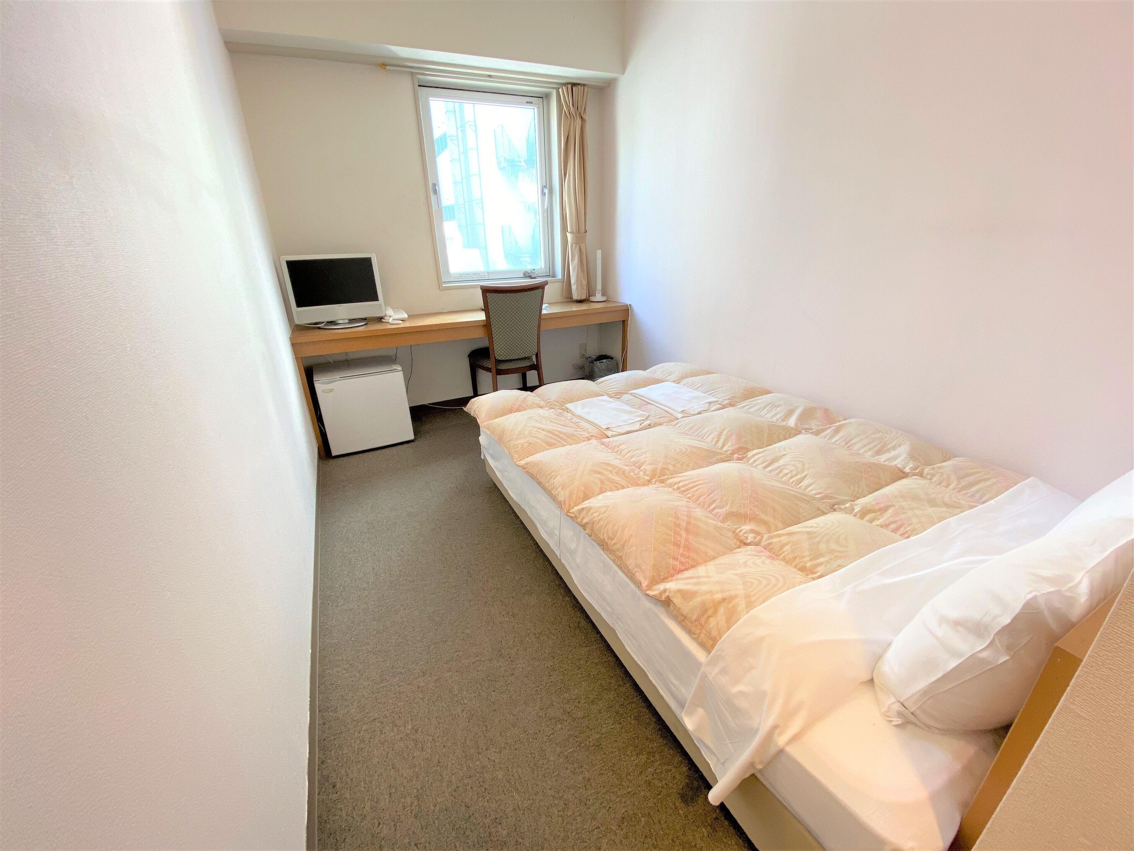 A small, neatly arranged bedroom with a bed, a desk with a computer, and a chair.