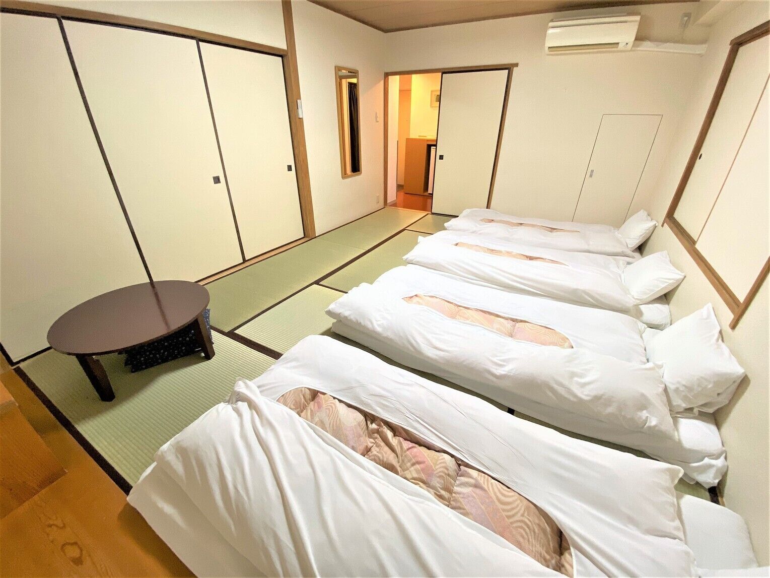 A traditional Japanese-style room with tatami flooring, a low table, and a bed with white bedding.