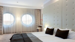 Een hotelkamer met een groot bed, een gestoffeerd hoofdeinde en uitzicht door dunne gordijnen.