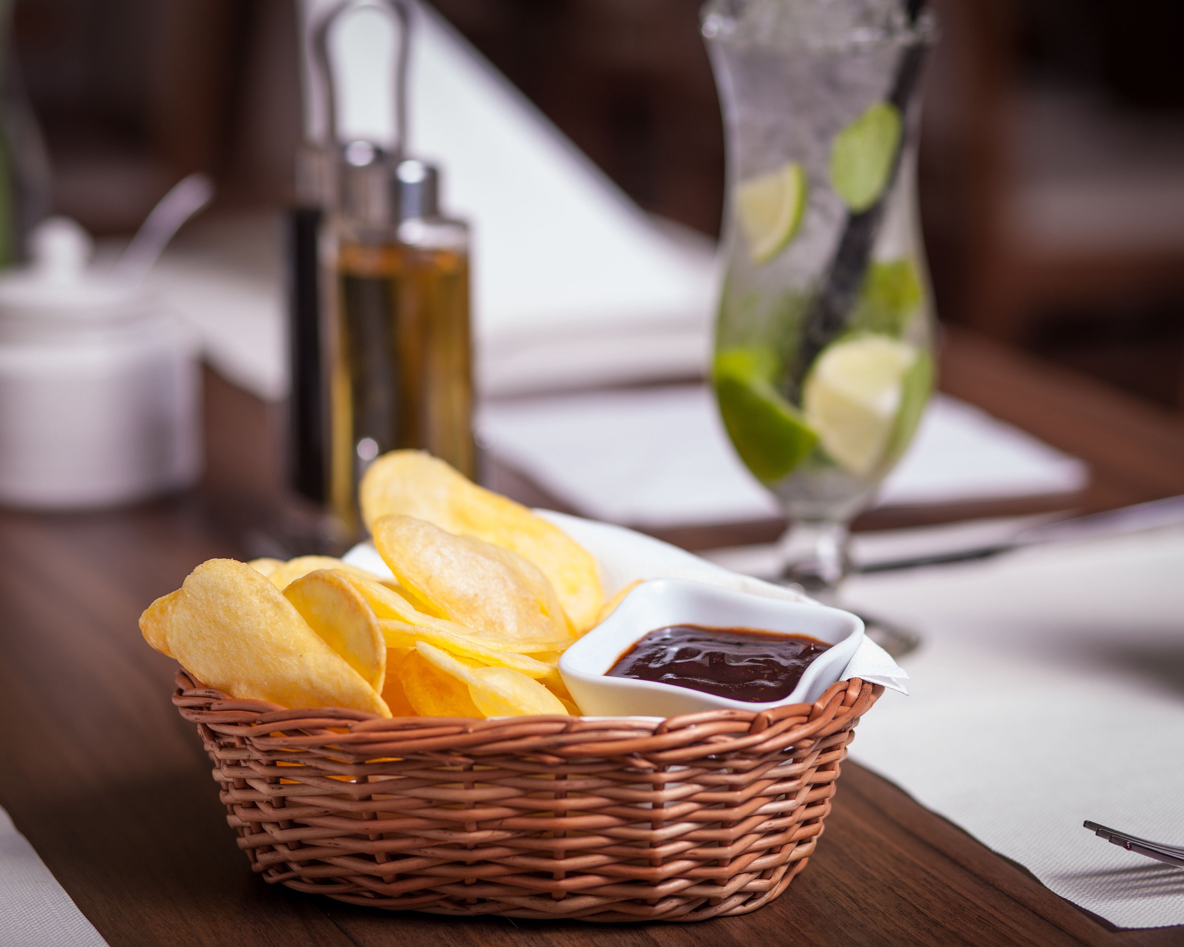 Un panier en osier rempli de chips et un petit bol de sauce pour tremper, posés sur une table en bois.