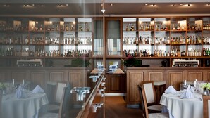 Een bar met drankflessen op de planken, een houten toog en zitplaatsen voor gasten.