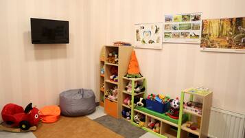 Une salle de jeux pour enfants avec une télévision, des peluches et des affiches éducatives.
