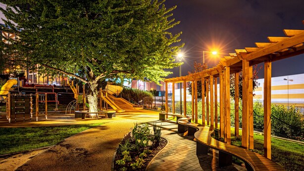 Een goed verlicht park met een speeltuin, bankjes en een overdekte looppad.