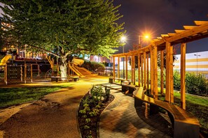 Ein gut beleuchteter Parkbereich mit Spielplatz, Bänken und einem überdachten Weg.