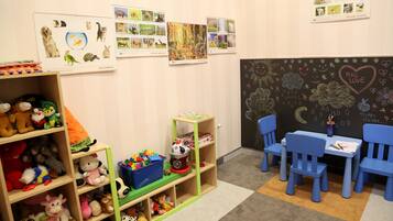 Un cuarto de juegos infantil con estantes llenos de peluches, una pizarra con dibujos y carteles educativos en la pared.