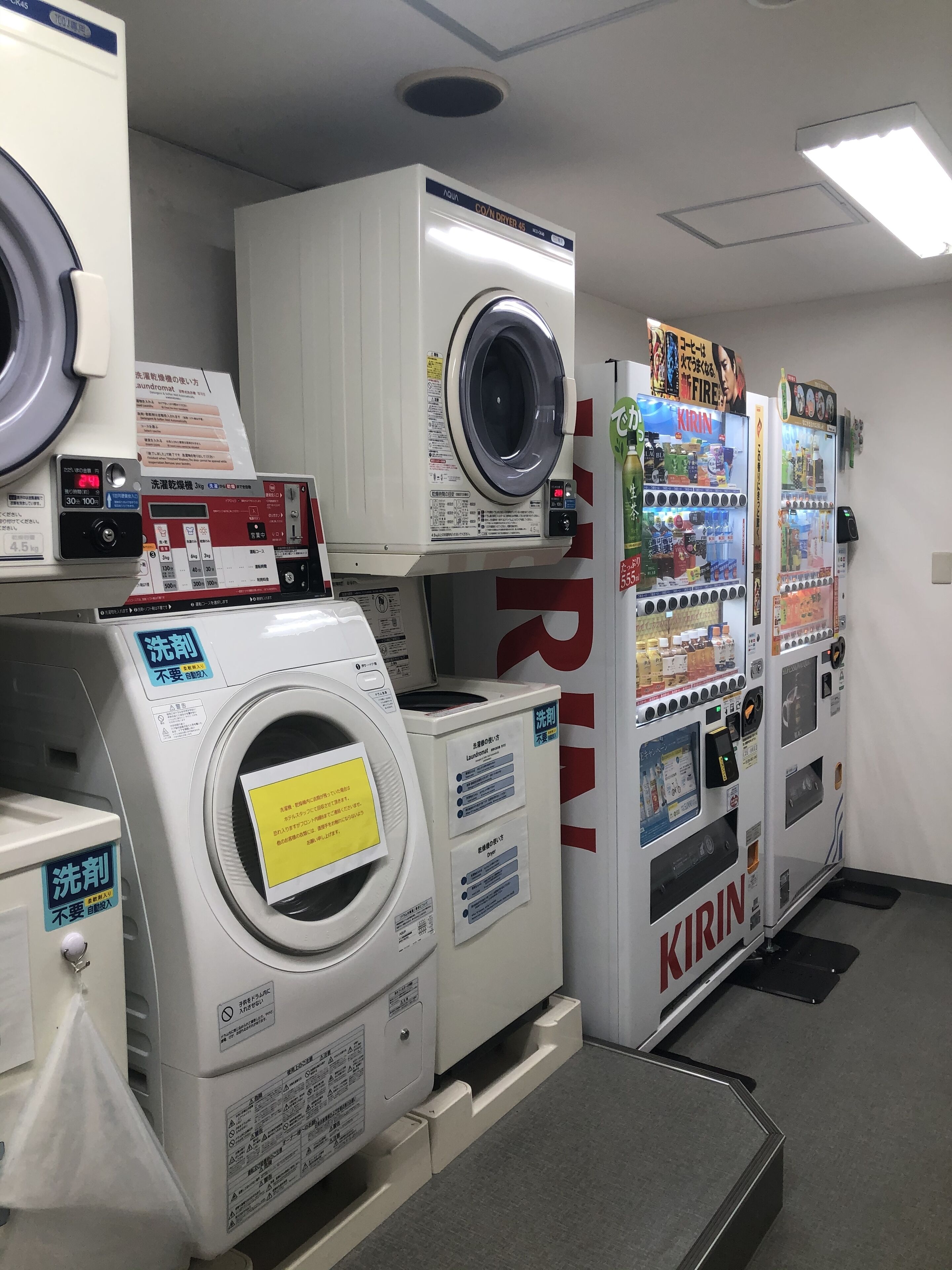 A laundromat with multiple washers and dryers, vending machines, and instructional signs.