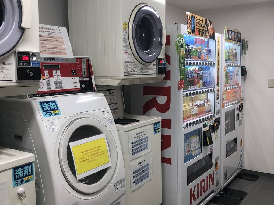 A laundromat with multiple washers and dryers, vending machines, and instructional signs.