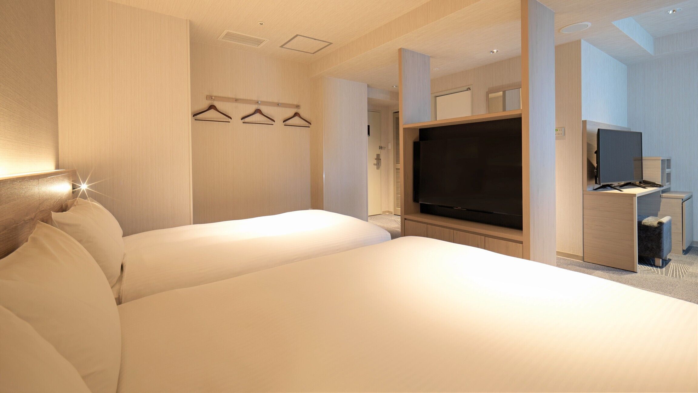A hotel room with a large bed, a flat-screen TV, a desk with a chair, and a coat rack with hangers.