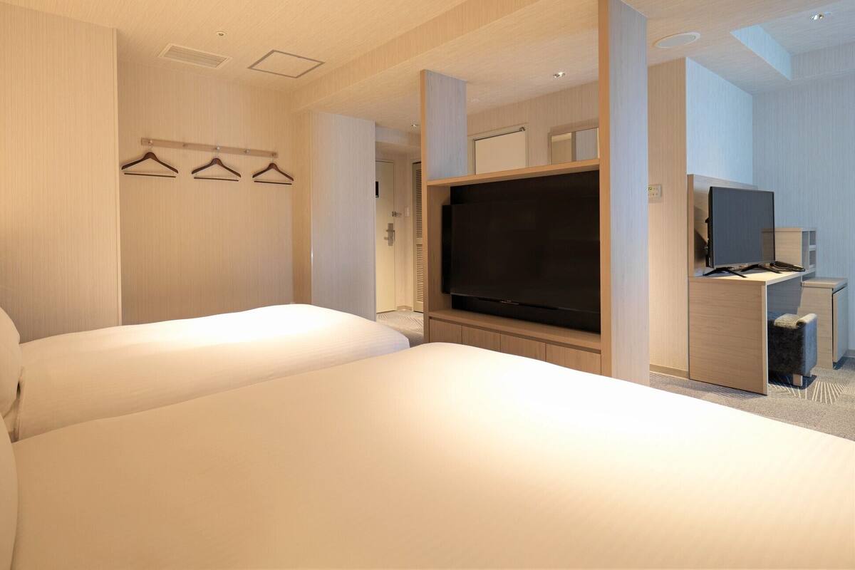A hotel room with a large bed, a flat-screen TV, a desk with a chair, and a coat rack with hangers.