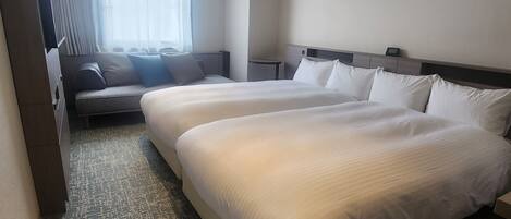 Hotelkamer met twee bedden, een slaapbank, een raam met gordijnen, een schilderij aan de muur en een vloerbedekking.
