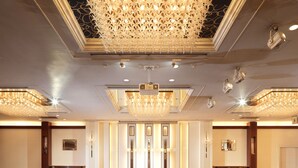 Um amplo hall de hotel com um lustre grande, diversas luminárias no teto e um tapete estampado.
