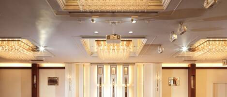 A spacious hotel lobby with a large chandelier, multiple ceiling lights, and a patterned carpet.