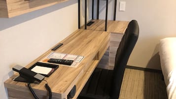 A hotel room with a wooden desk, a black office chair, a telephone, and a flat-screen TV mounted on the wall.