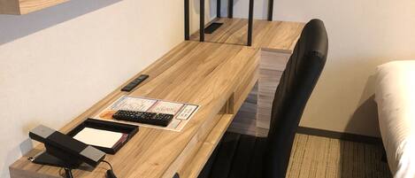 A hotel room with a wooden desk, a black office chair, a telephone, and a flat-screen TV mounted on the wall.